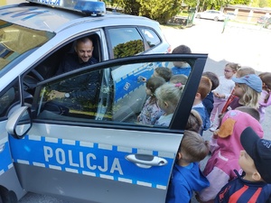 policjant uczy dzieci prawidłowych zachowań na drodze w tle teren przedszkola
