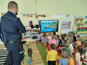 policjant uczy dzieci prawidłowych zachowań na drodze w tle teren przedszkola