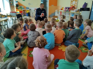 policjant uczy dzieci prawidłowych zachowań na drodze w tle teren przedszkola