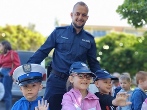 policjant uczy dzieci prawidłowych zachowań na drodze w tle teren przedszkola