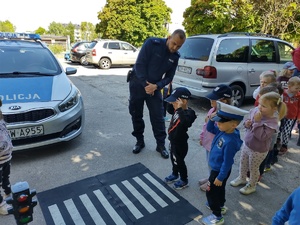 policjant uczy dzieci prawidłowych zachowań na drodze w tle teren przedszkola