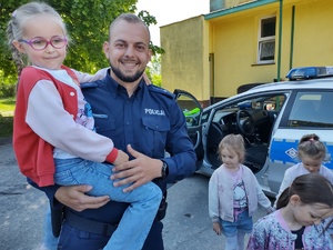 policjant uczy dzieci prawidłowych zachowań na drodze w tle teren przedszkola