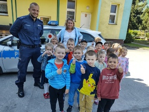 policjant uczy dzieci prawidłowych zachowań na drodze w tle teren przedszkola