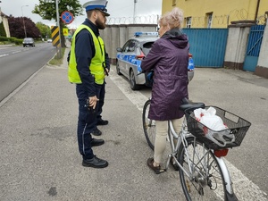 POLICJANCI ROZMAWIAJĄ Z ROWERZYSTAMI W TLE OGRODZENIE JEDNOSTKI I ULICA