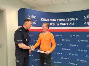 komendant wręcza podziękowania mężczyźnie w tle baner z logo policji