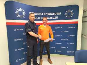 komendant wręcza podziękowania mężczyźnie w tle baner z logo policji
