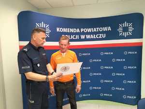 komendant wręcza podziękowania mężczyźnie w tle baner z logo policji
