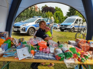 policjanci bawią się z dziećmi w tle teren zewnętrzny jednostki, radiowozy, banery, dzieci i dorośli
