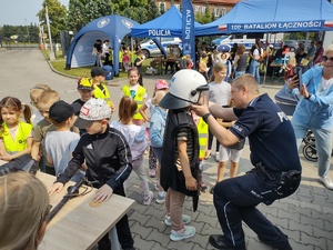 policjanci bawią się z dziećmi w tle teren zewnętrzny jednostki, radiowozy, banery, dzieci i dorośli