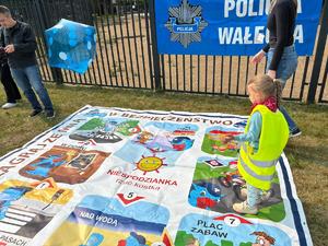 policjanci bawią się z dziećmi w tle teren zewnętrzny jednostki, radiowozy, banery, dzieci i dorośli
