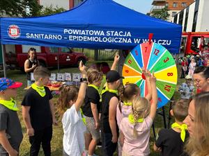 policjanci bawią się z dziećmi w tle teren zewnętrzny jednostki, radiowozy, banery, dzieci i dorośli
