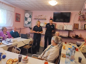 policjanci rozmawiają z seniorami w tle pomieszczenie