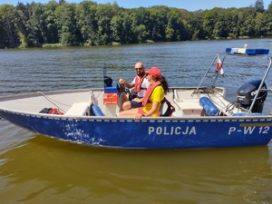 policjant i ratowniczka WOPR kontrolują jezioro w tle las