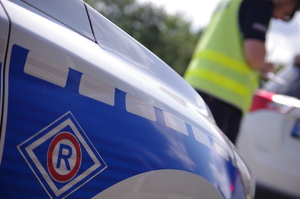 drzwi od radiowozu w tle policjant w kamizelce kontroluje pojazd