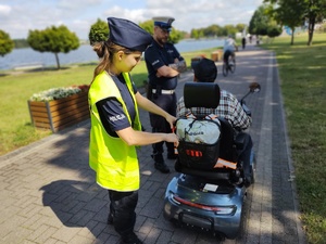policjanci wręczają odblaski w tle promenada jeziora