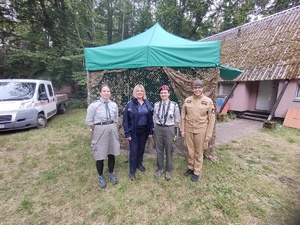 policjanci i strażacy rozmawiają z harcerzami i zuchami w tle las i namioty
