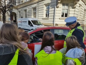 policjant prowadzi działania z uczniami w tle ulica i pojazdy