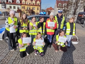 policjant prowadzi działania z uczniami w tle ulica i pojazdy