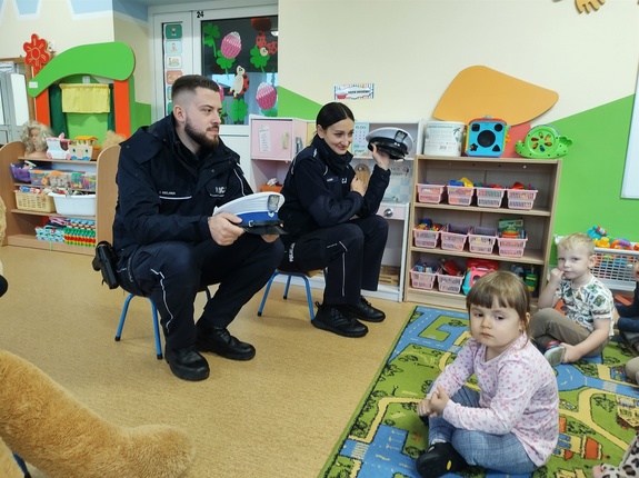 policjanci rozmawiają z przedszkolakami w tle sala