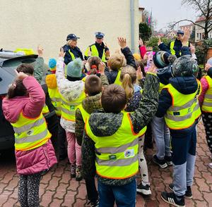 Policjanci przed posterunkiem z uczniami. W tle ulica