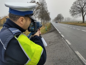 policjant sprawdza prędkość pojazdu, w tle ulica i pojazd