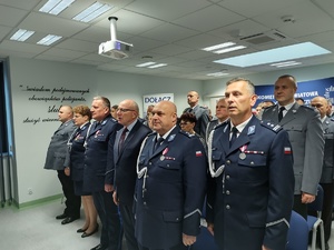 Policjanci na uroczystej zbiórce w tle banery i flaga Polski