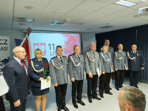 Policjanci na uroczystej zbiórce w tle banery i flaga Polski