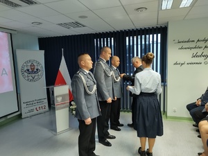 Policjanci na uroczystej zbiórce w tle banery i flaga Polski