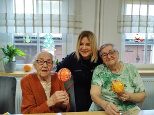 policjantka obejmuje dwie seniorki, które trzymają bombki w tle okno