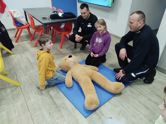 policjant uczy udzielania pierwszej pomocy, w tle sala