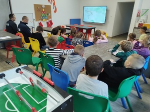 policjant uczy udzielania pierwszej pomocy, w tle sal