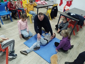 policjant uczy udzielania pierwszej pomocy, w tle sal