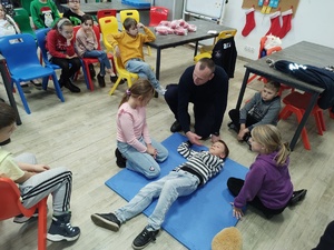 policjant uczy udzielania pierwszej pomocy, w tle sal