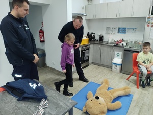 policjant uczy udzielania pierwszej pomocy, w tle sal