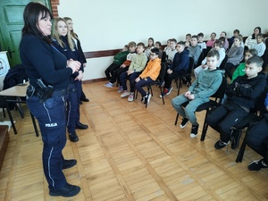 Policjantki i pracownik sanepidu rozmawiają z uczniami w tle sala lekcyjna