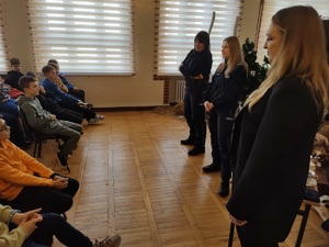 Policjantki i pracownik sanepidu rozmawiają z uczniami w tle sala lekcyjna