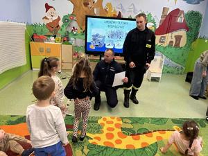 policjanci rozmawiają z przedszkolakami w tle sala