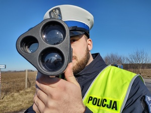 policjant dokonuje pomiaru prędkości,  w tle zarośla
