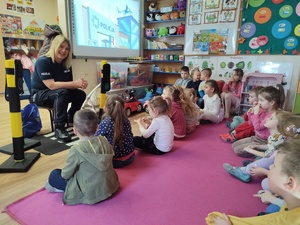 policjantka rozmawia z przedszkolakami w tle sala i ekran na ścianie z bajką