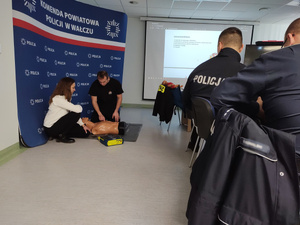 policjanci uczestniczą w szkoleniu w tle tablica z prezentacją, instruktor i fantomy