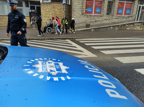 policjanci i cywile pomagają mężczyźnie na wózku inwalidzkim w tle ulica i zabudowania