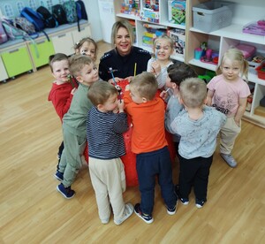 policjantka uczy dzieci pierwszej pomocy w tle inne dzieci i wyposażenie sali