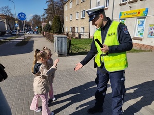 policjant wręcza odblaski w tle zabudowania i radiowóz