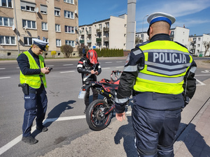 policjanci kontrolują rowerzystów i motocyklistów w tle zabudowania i ulica