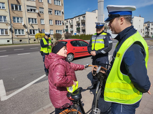 policjanci kontrolują rowerzystów i motocyklistów w tle zabudowania i ulica