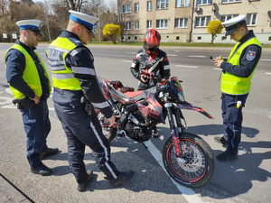 policjanci kontrolują rowerzystów i motocyklistów w tle zabudowania i ulica