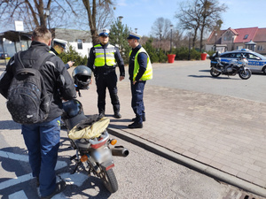 policjanci kontrolują rowerzystów i motocyklistów w tle zabudowania i ulica