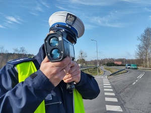policjant odwrócony tyłem dokonuje pomiaru prędkości w tle ulica