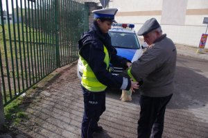 Policjantka zakłada odblask na przedramię pieszemu, w tle radiowóz
