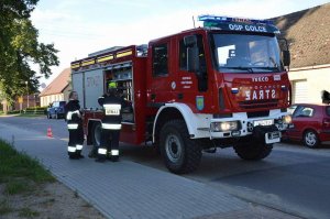 policjantka- strażak w zakończonej akcji stoi z kolegą strażakiem przy wozie bojowym, w tle inne cywilne auta na drodze